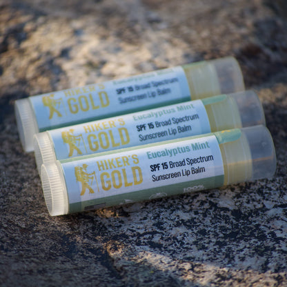 Three Hiker's Gold sunscreen lip balms on a textured surface