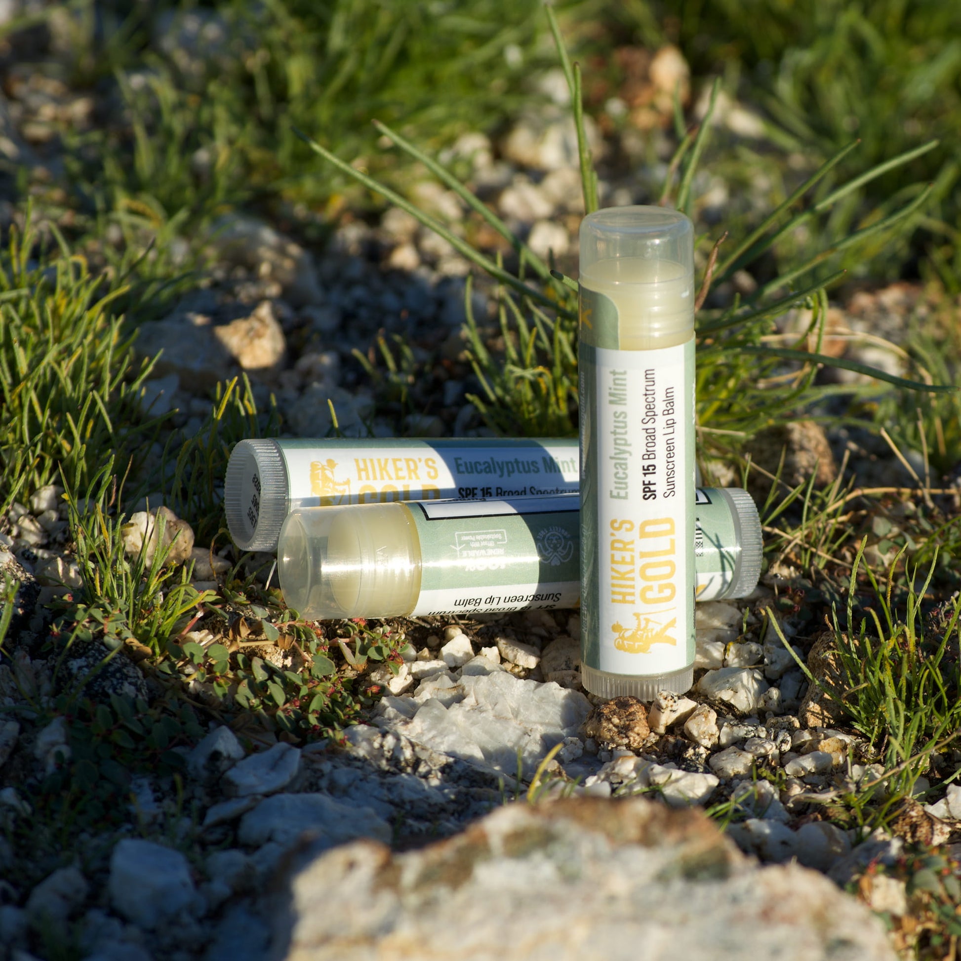 Three lip balm tubes on a rocky and grassy surface