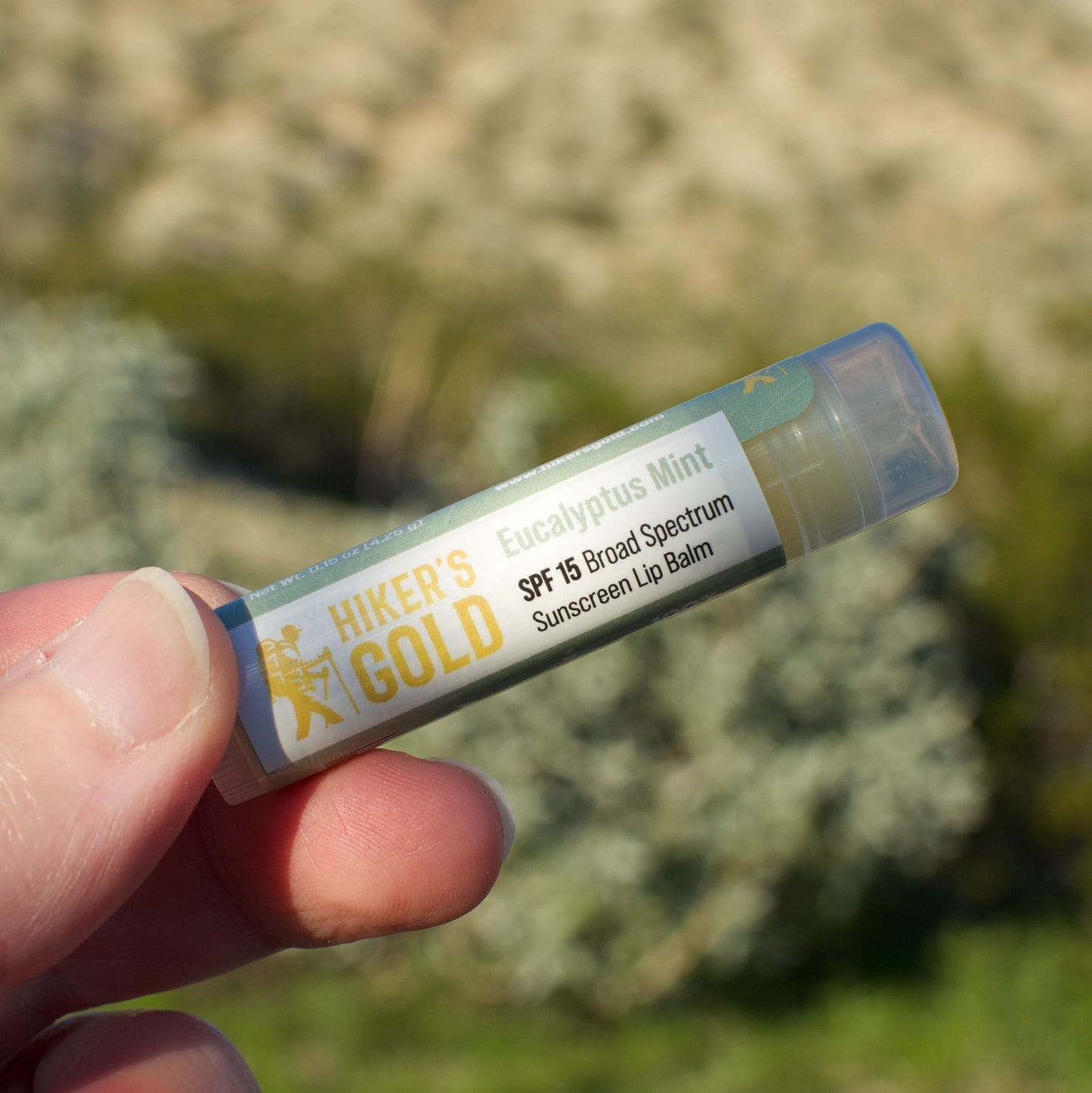 Hiker's Gold lip balm tube held in a hand with a blurred natural background