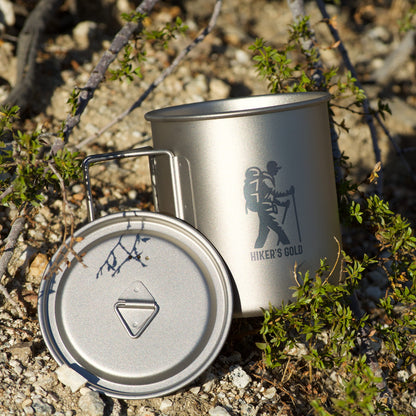 Metal camping mug with lid on a rocky ground with greenery